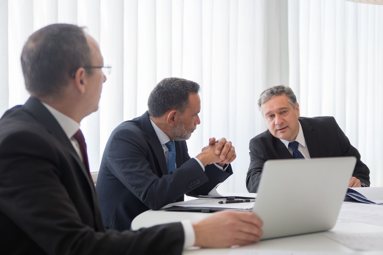 Three businessmen collaborating during a meeting around a laptop in a bright office.